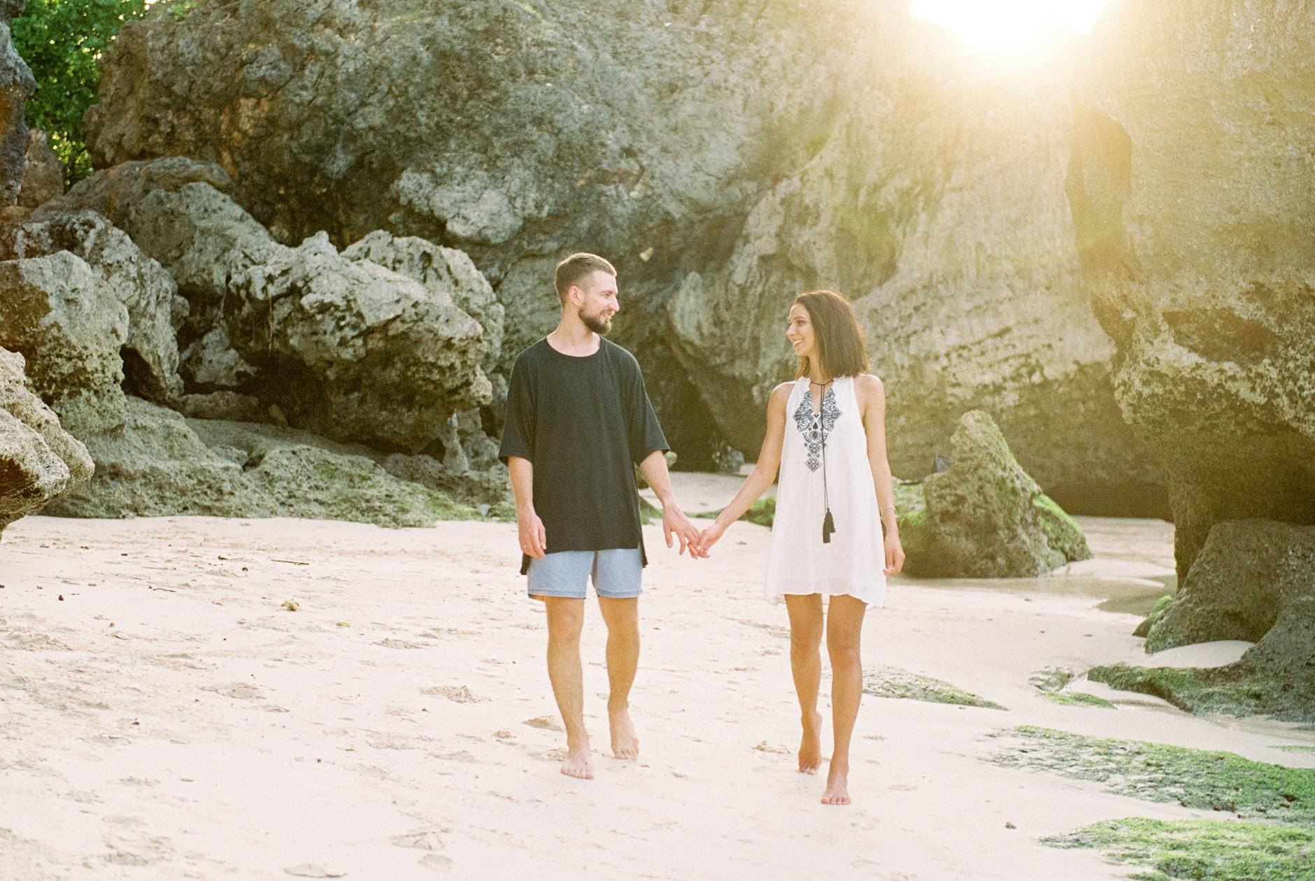 Para trzymająca się za ręce idzie boso po słonecznej plaży na Bali