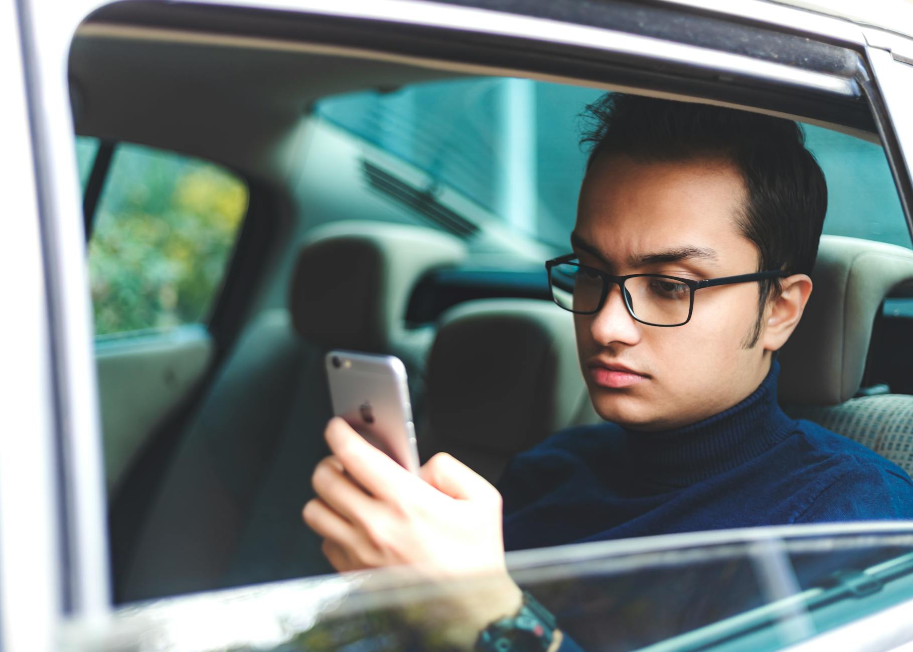 Młody mężczyzna w okularach korzysta ze smartfona w zaparkowanym aucie
